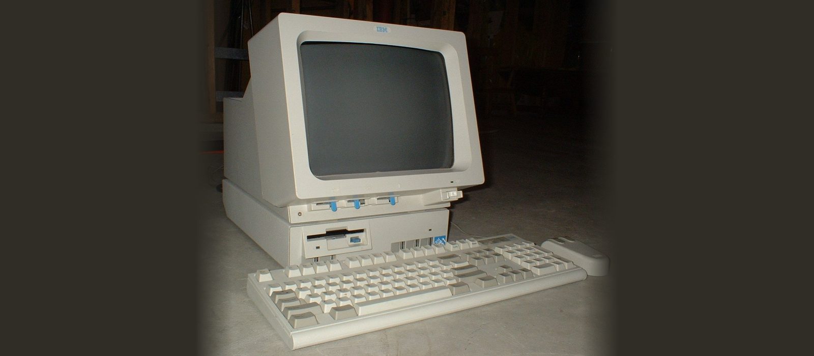 An IBM PS/1 computer with its monitor, keyboard and mouse, photographed in low light