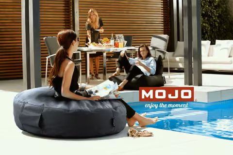 A woman reading on a black Mojo bean bag beside a pool